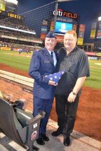 New York City, Monday, August 20, 2012: Mets legend Rusty Staub (right) presents flag to Msgr. Mark Rowan, Ch Col AFRC, “Veteran of the Game” between Mets and Rockies. Photo courtesy New York Mets.